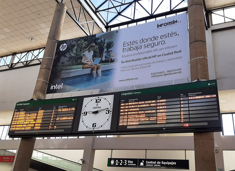 Publicidad de Inforein en la estación AVE de Ciudad Real con reloj y tableros de información de trenes.