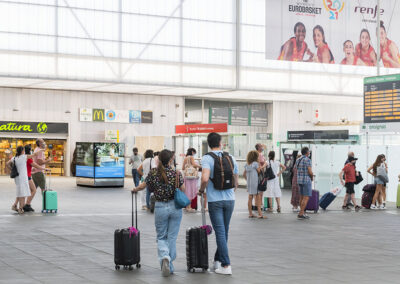 Pasajeros en la estación AVE de Valencia con publicidad de Inforein y anuncios de Renfe en el fondo.