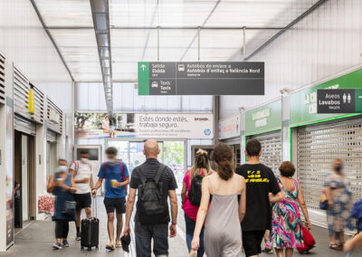 Pasillo de estación del AVE con personas y publicidad de Inforein en la parte superior.