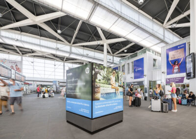 Publicidad de Inforein en la estación de AVE de Valencia con pasajeros en movimiento.